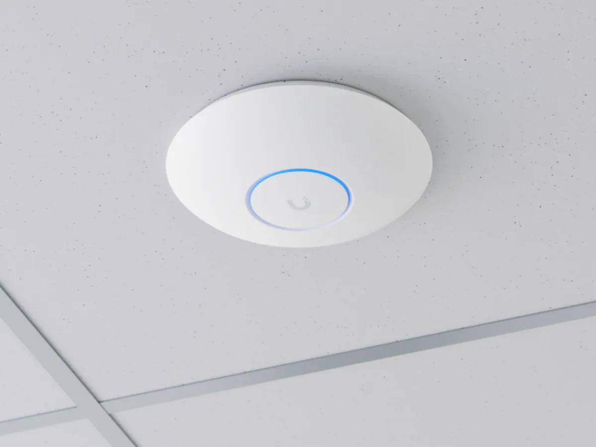 A UniFi access point mounted on a drop ceiling, its ring light glowing blue